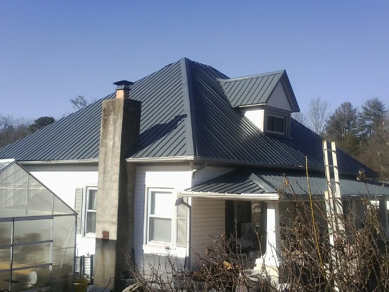 Dark blue standing seam metal roof on a white farmhouse with dormer — Slate & Tile Roof Repair by Roofing Brothers in Bagdad