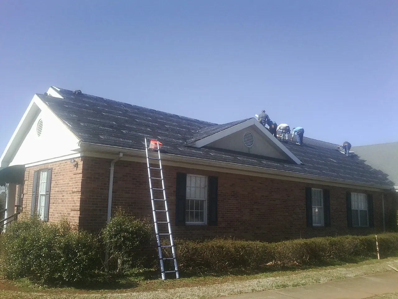 Crew tearing shingles off a brick ranch roof with a ladder set — Metal Roof Repair work by our crew in Bagdad