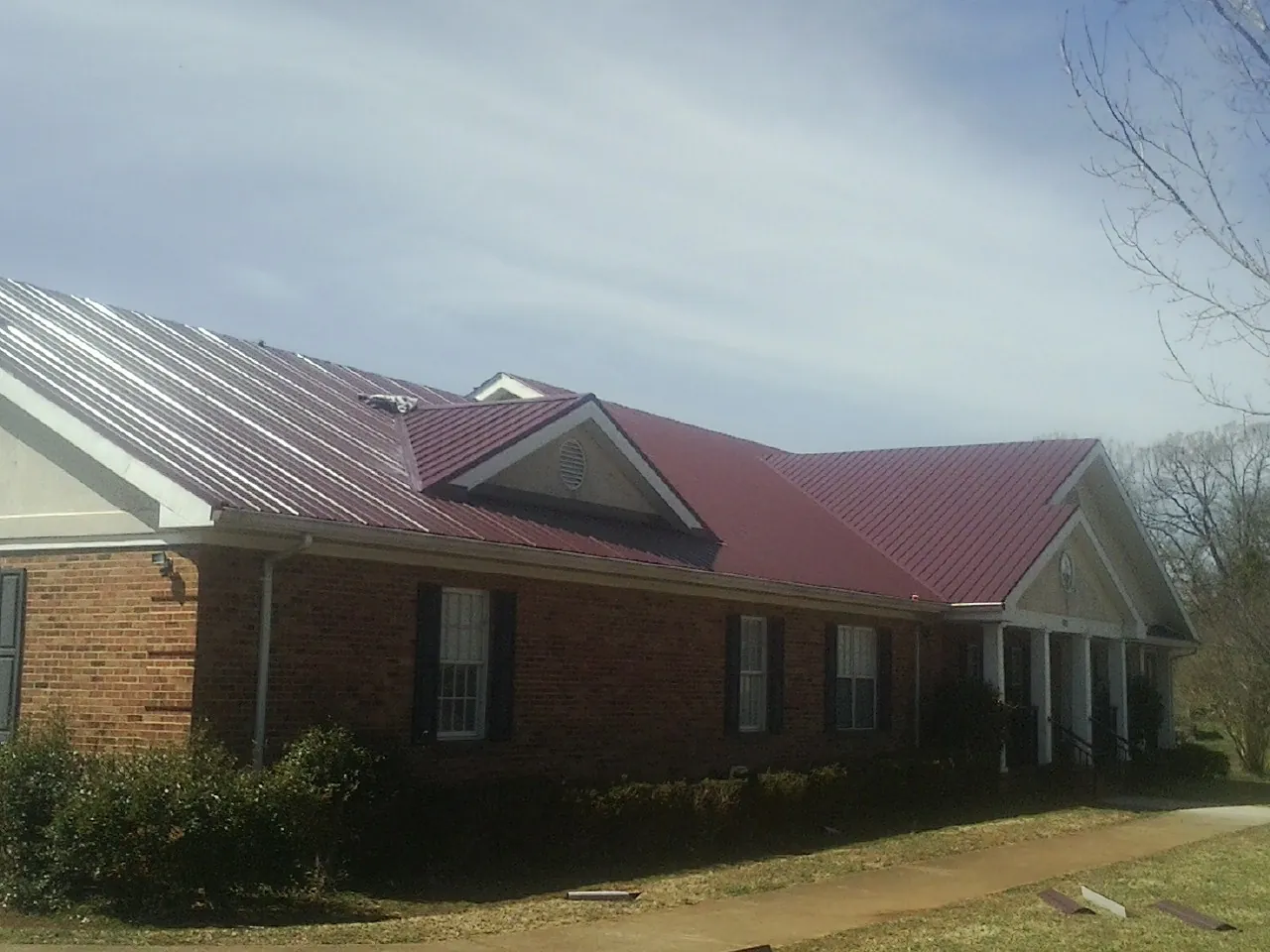 Red metal roof with gabled entries on a long brick building, from a Hail Damage Roof Repair job in Bagdad