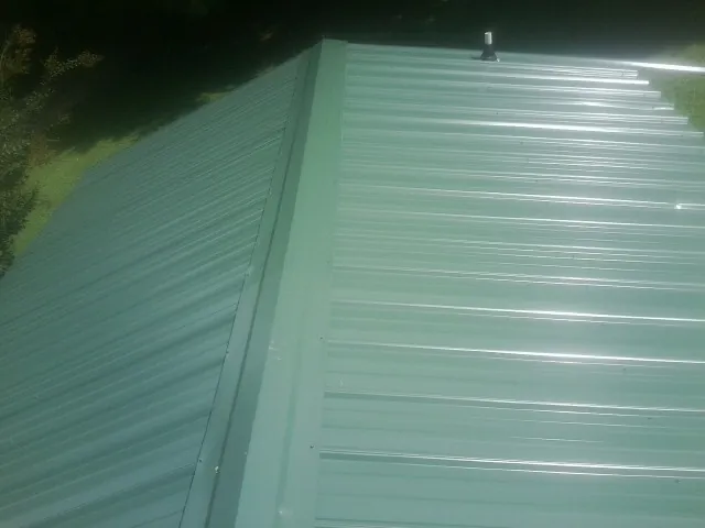 New green metal panels meeting at the ridge of a roof — Flat Roof Repair work by our crew in Bagdad