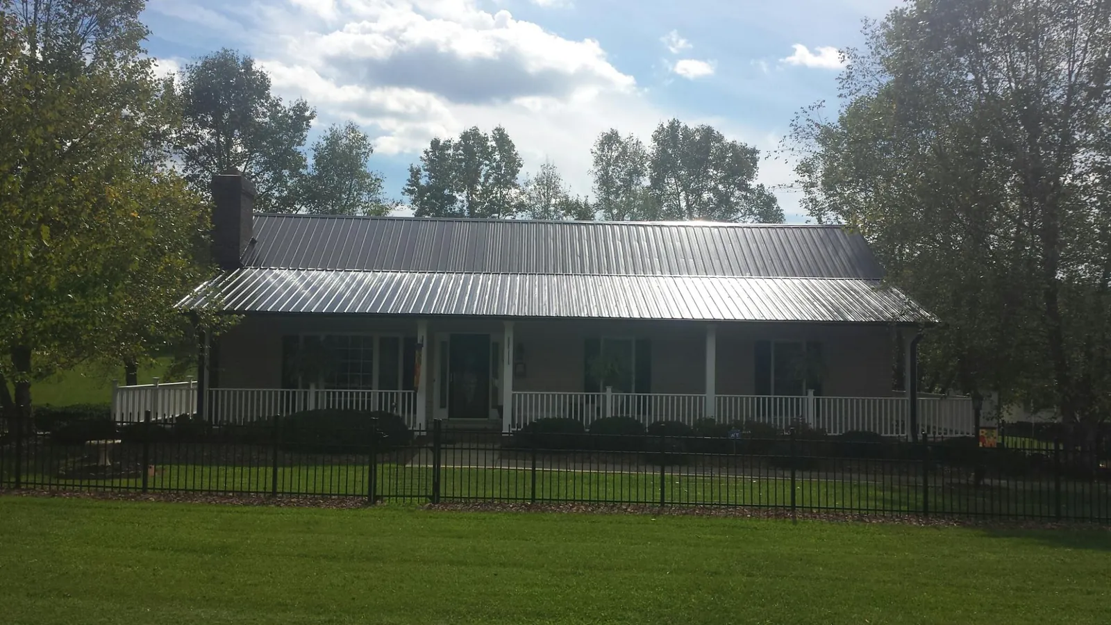 Gray metal roof on a brick ranch with a full width front porch — Gutter Guard Installation work by our crew in Bagdad