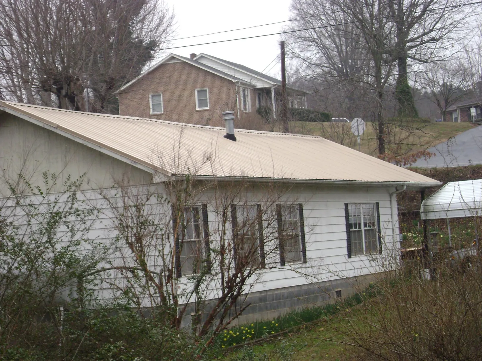 Tan metal roof on a white sided house set into a hillside — Commercial Roofing by Roofing Brothers in Bagdad