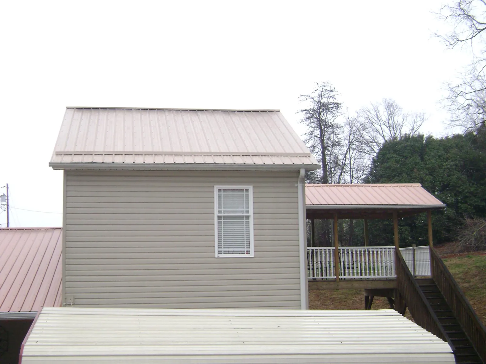Tan metal roofs on a two story addition and attached porch, from a Roof Replacement job in Bagdad